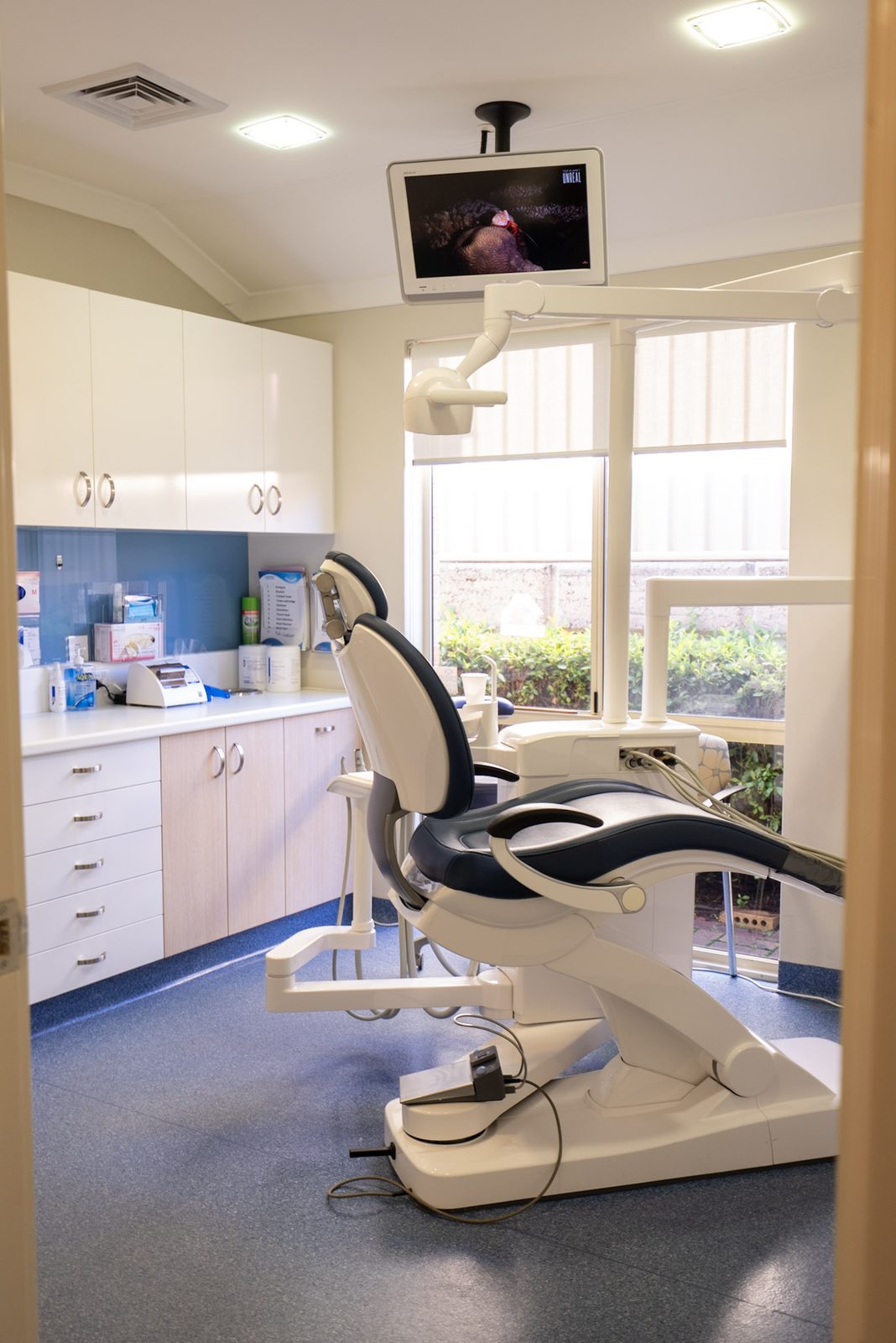 Dental surgery room with chair, overhead light and ceiling-mounted television at Australind Dental Centre